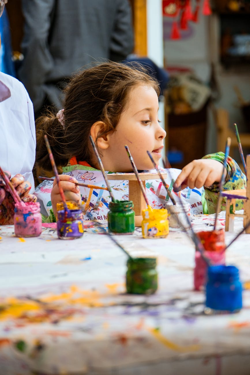 A young girl painting with vibrant colors in an art class, surrounded by paint pots.